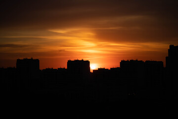 Fototapeta na wymiar Big city in the rays of the sunset. High-rise black houses and red fiery sky.