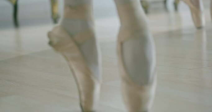 Crop ballerinas dancing on floor. Unrecognizable dancers in pointe shoes dancing ballet gracefully on parquet floor in studio - slow motion