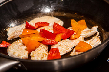Slices of chicken breast are fried with vegetables: peppers, tomatoes, pea pods.