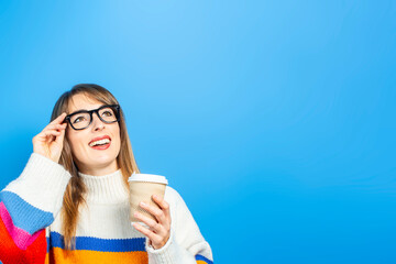  young girl holds a cardboard cup with coffee and shows emotions, joy, happiness on a blue background. Banner