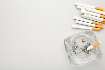 Cigarette butts with ash in ashtray on grey background.