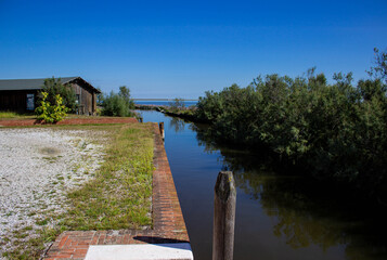 Canal in the Venetian lagoon with bricole and a brick wall. Codevigo, Padua, Italy.