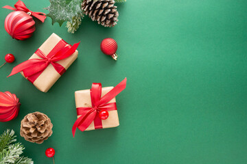 Christmas green background with winter decorations, gift boxes, fir branches, pine cones and red baubles. Copy space, flat lay.