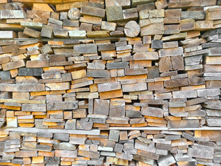 Background from multi-colored ends of wooden bars of different sizes and shapes. Wood texture. Woodpile in the village. Harvesting firewood