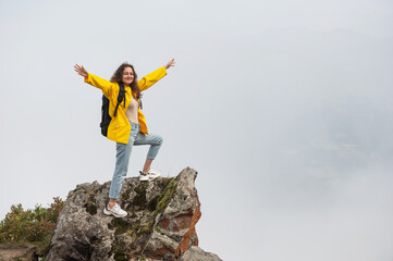 Happy caucasian woman on the top of the mountain raising hands in the air against cloud