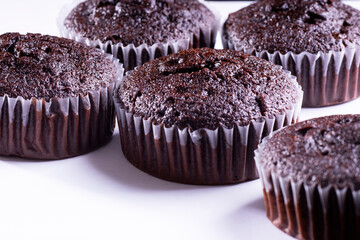 Set of plain dark chocolate cupcakes in paper cups on white background - side View
