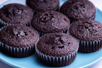 Set of plain dark chocolate cupcakes in paper cups on blue dish on white background - side View
