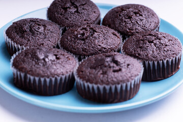 Set of plain dark chocolate cupcakes in paper cups on blue dish on white background - side View
