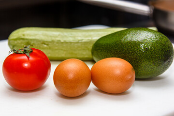 Raw eggs, tomatoes, avocado and zucchini are on a white Board