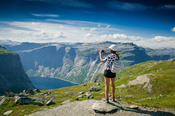 girl photographing the nature. tourist in a white cap and with a backpack in the mountains of Norway. Girl tourist  photographing on the edge of a cliff