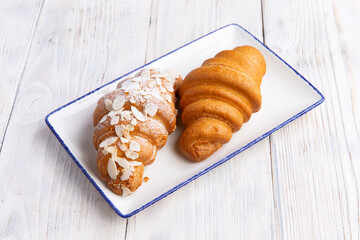 Two croissants in a plate on a light board