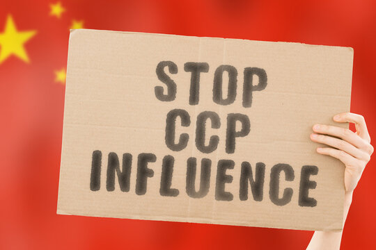 The phrase " Stop CCP influence " on a banner in men's hand with blurred Chinese flag on the background. Communist party. China. Control. Government. Politics. Authority