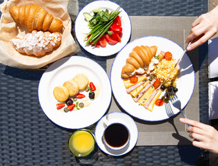 Breakfast outside. Fried eggs, coffee, croissants. Hands in the frame.