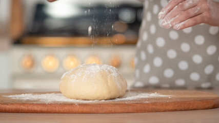 Knead dough, hand dough and flour close-up. A pastry chef in a grey polka-dot apron.