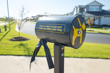 A public dog waste bag dispenser in a suburban park with the text .'please take a bag and clean after your dog' and a blurry view of some houses as background.  Melbourne, VIC Australia.