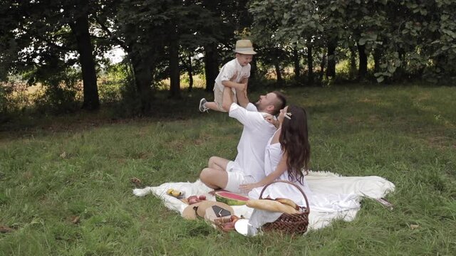 Long-haired young woman and her bearded dark-haired husband playing with their joyful son in a forest meadow. Family recreation concept