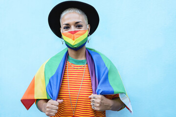 Portrait of gay young woman with mask wearing a rainbow flag - Lgbt concept - Focus on face