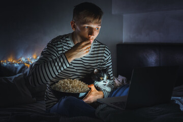 young man with black cat watching a movie eating popcorn on TV at home. Movie night. Relax,rest...