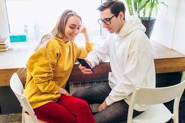 The guy and the girl look at the smartphone and communicate.