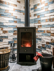 Modern wood burning stove. Tiled wall behind, stove with fire burning inside, cosy and warm interior scene, heating in winter.
