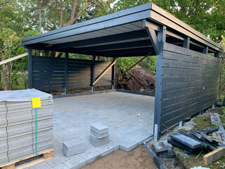 Paving stones, which stand on pallets, are laid in a carport