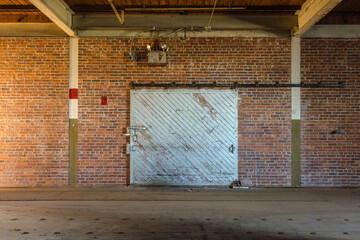 Empty open space with long brick wall and barn door in an abandoned factory