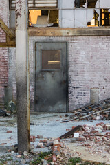 Vertical shot of metal door with brick and debris of abandoned factory