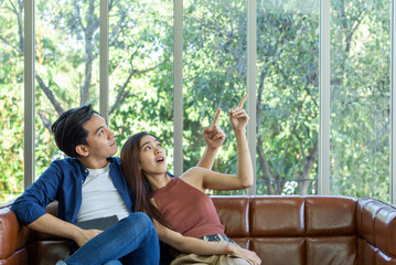 Obraz premium Young couples spend holidays in the living room. The young man wore comfortable clothes and the girlfriend pointed finger and looked in the same direction.