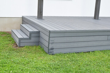 Part of dark gray or anthracite wpc composite meterial terrace deck with stairs  in backyard green grass outdoors.
