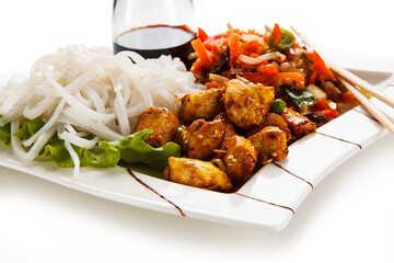 Chicken nuggets, white white rice noodles, soy sauce and vegetables served on white background