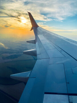 View from airplane window and the wing with sunset sky over fluffy clouds, flying and traveling concept background