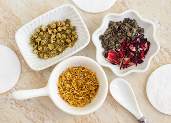 Small white bowls with dried chamomile, marigold flowers, green tea, hibiscus. Natural skin care, homemade spa, beauty treatment recipe. Herbal medicine, zero waste, skip care concept. Top view
