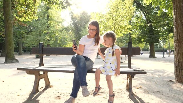 Woman mother makes phone photo selfie picture of her child daughter eat ice cream family together in city park sit on bench having fun