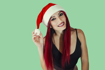 Christmas Woman. Beauty Model Girl in Santa Hat isolated on green Background. Funny Laughing Surprised Woman Portrait. Open Mouth. True Emotions. Red Lips and Manicure. Beautiful Holiday Makeup.