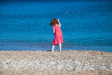 Little redhead girl throwing stones in the sea