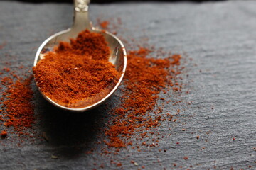 A close up photograph of cayenne pepper spices on a teaspoon, on a slate counter