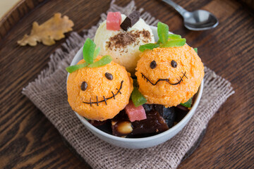 Halloween dessert in a white cup. It consists of ice cream in the form of ghost pumpkins. Creative food for the holiday and a good mood.