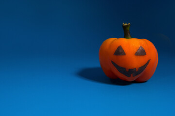 Orange peppers with scary face looking like a pumpkin on a blue background with copyspace. Halloween theme.