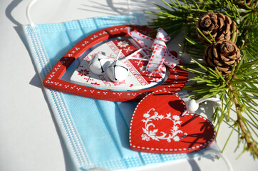 Christmas branch with cones decorated with red hearts on the background of a protective mask.