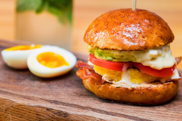 Close up tall tasty burger with cheese, tomatoes and omelet served on serving board