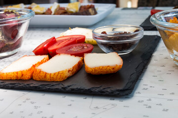 Different kinds of delicious and tasty cheese, with cherry tomatoes and isolated black greek olives. More food like italian bruschetta and hummus in background