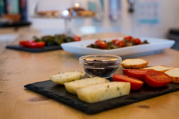 Different kinds of delicious and tasty cheese, with cherry tomatoes and isolated black greek olives. More food like italian bruschetta and hummus in background