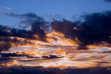 Fototapeta premium The sky before a thunderstorm. Golden sunlight against dark purple clouds.