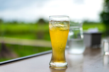 Beer in glass on wooden table with blurred city park on background, natural background with bokeh