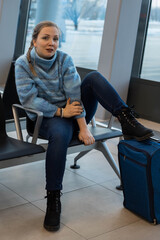 An ill-mannered woman sits in an airport waiting room, one leg thrown vulgarly over her suitcase and glares defiantly at the camera - obrazy, fototapety, plakaty
