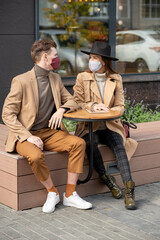 Young restful couple in protective masks and casualwear relaxing outdoors