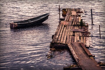 View of the river with a lonely fishing boat moored to an old wooden pier. Vintage style.