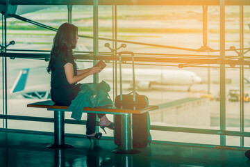 Fototapeta premium Asian woman at international airport, checking passport, luggage and waiting for her flight and background blur airplane, view from airport terminal. (vintage color tone, lens blur effect)