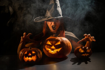 The evil witch casts a spell on pumpkins. Portrait of a woman in a carnival halloween costume in...