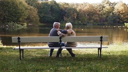 Elderly gray haired couple siting on the bench near the river on autumn day. Romance and old age....